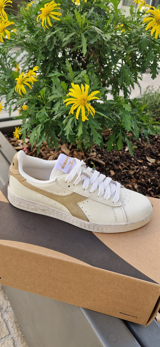 Basket Diadora Game L basse en cuir blanc avec logo doré clair texturé, posée sur sa boîte.