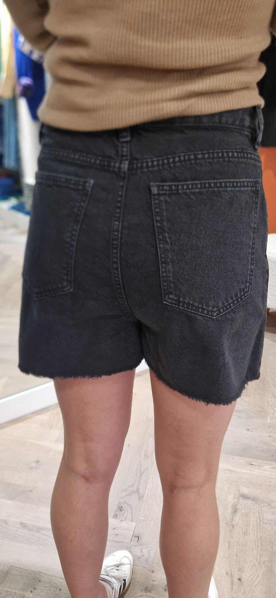 Vue de dos du short en jean noir de la marque Acquaverde. Taille haute marquée et bas effiloché.
