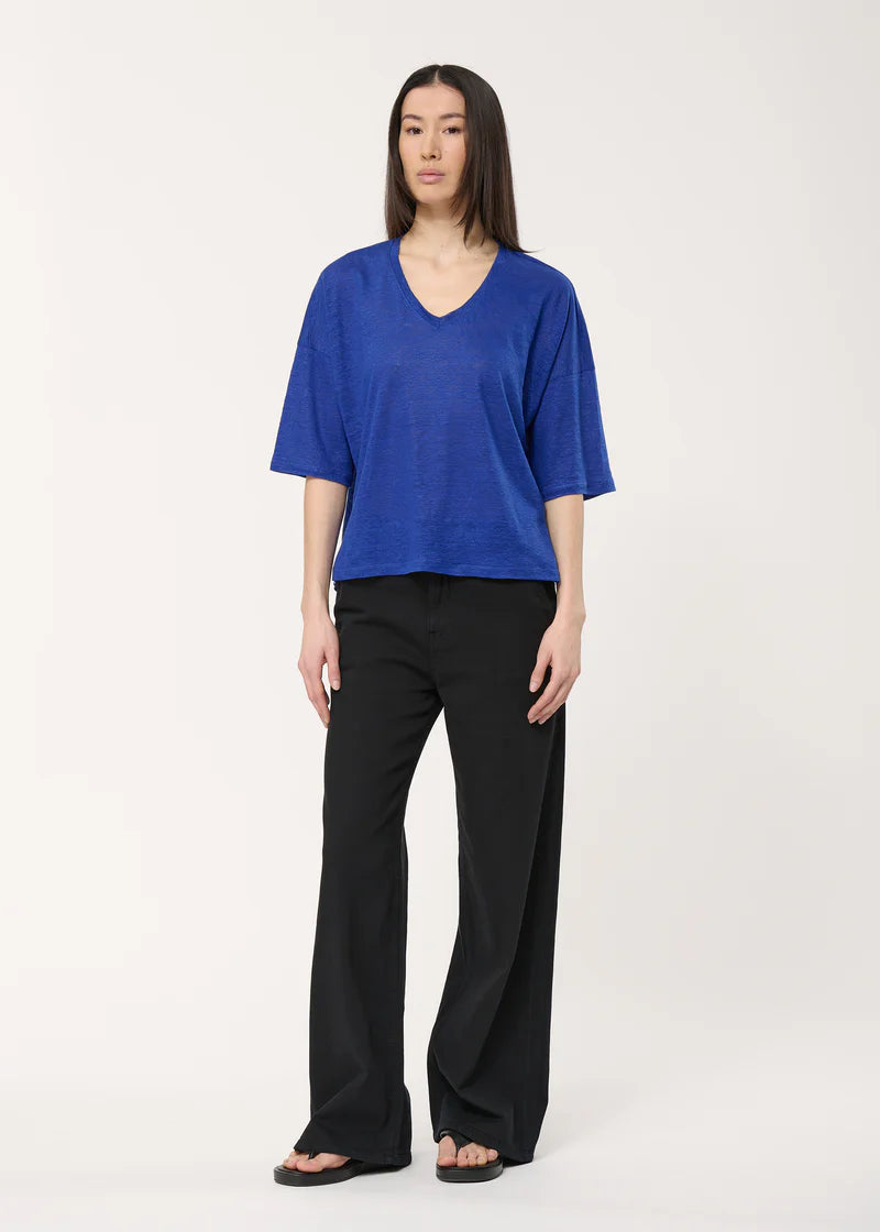 T-shirt Berlin Humility manches 3/4 en bleu électrique, coupe fluide et col en V, porté avec un pantalon noir large.