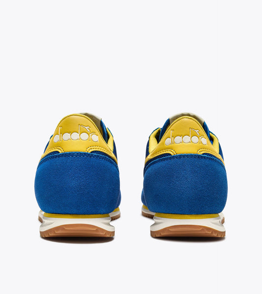 Vue arrière des baskets Cross Diadora. Talon jaune avec logo blanc et semelle bicolore.