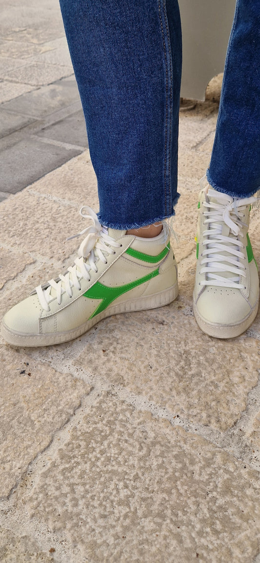 Baskets montantes Diadora Game L High, blanches avec logo vert fluo, portées.
