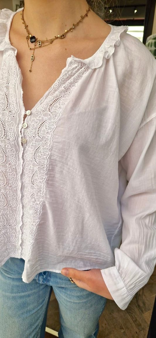 Zoom sur la blouse blanche de chez Bella jones. Elle a des broderies anglaises sur le devant et un petit volant sur le col en V. Manches longues.