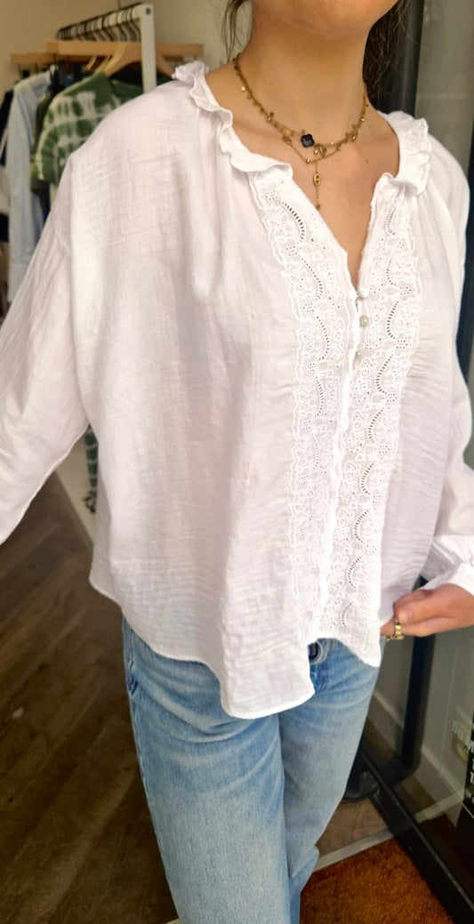 Vue de face de la blouse blanche de chez Bella jones. Elle a des broderies anglaises sur le devant et un petit volant sur le col en V.