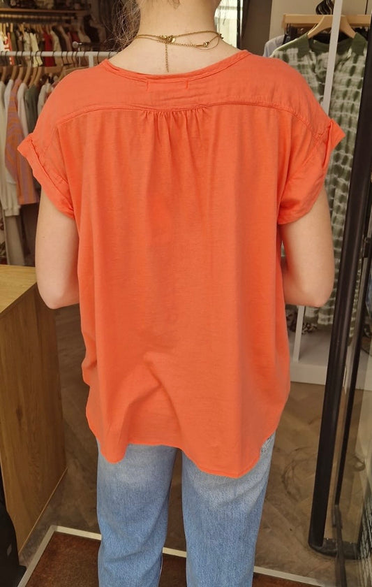 Vue de dos d'une femme portant la blouse orange fluide sans manches de chez Bella Jones. Elle possède un effet froncé dans le dos.