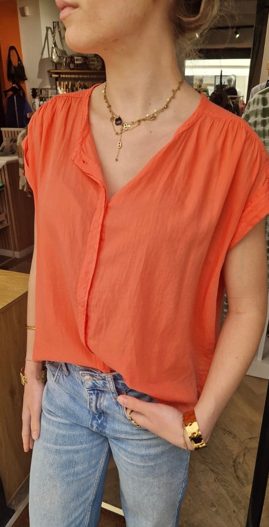 Femme portant la blouse orange fluide sans manches de chez Bella Jones. Elle a un col V.