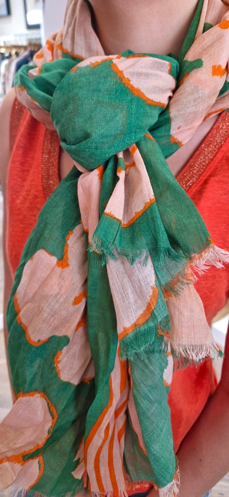 Femme portant une écharpe légère de chez Bella Jones aux motifs fleuris verts, orange et écru et noué autour du cou.