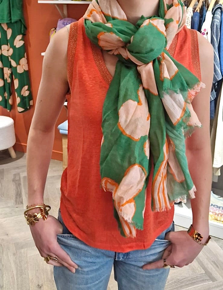 Femme portant une écharpe légère de chez Bella Jones aux motifs fleuris verts, orange et écru et noué autour du cou.