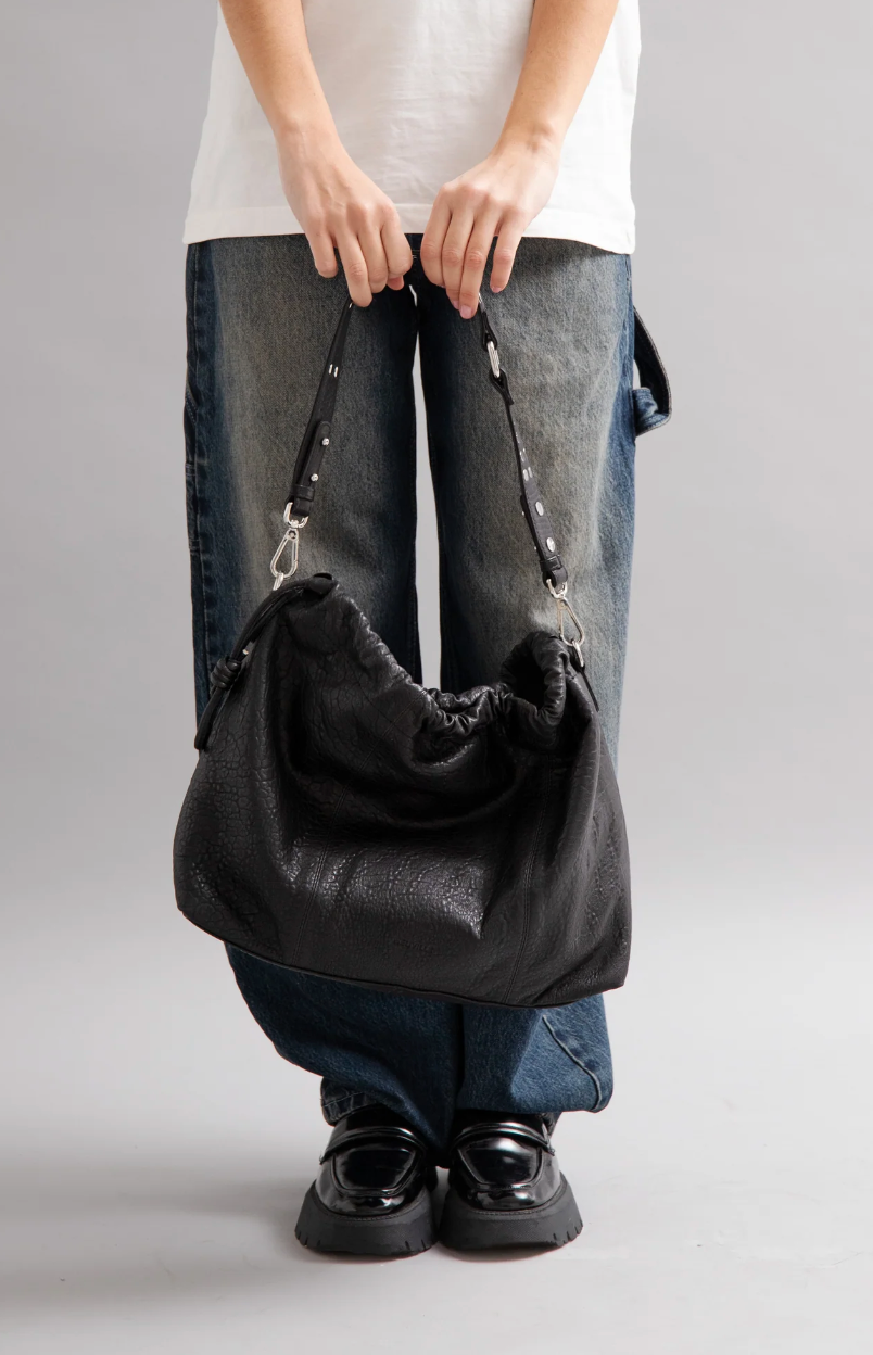 Sac Elliot bubble noir Neuville en cuir porté à la main. Vue en situation qui montre la taille réelle du sac et la bandoulière cloutée.